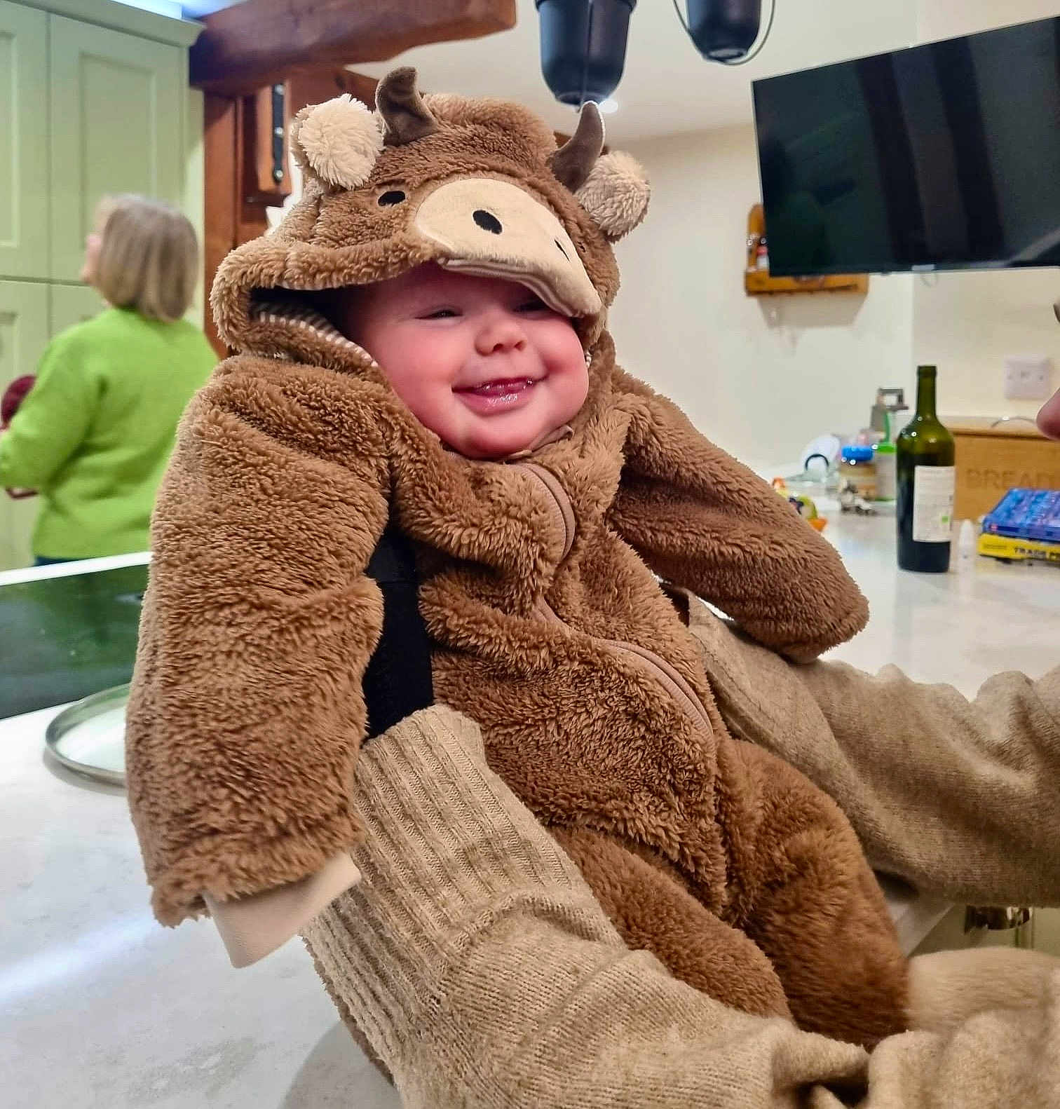 Emilia joined the competition — help win amazing prizes! baby, child, smile, happy, fuzzy_clothing, onesie, costume, indoor, kitchen, person, holding, warm_clothing, cute, cheerful, face, headwear, soft_texture, adult, background, home