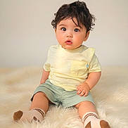 Ruth joined the competition — help win amazing prizes! baby, banner, birthday, child, cream_background, curly_hair, eight_months, fluffy_rug, gold, indoors, infant, looking_at_camera, portrait, shirt, shorts, sitting, socks, sparkle, studio_photo, surprised_expression