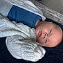 baby, infant, face, knitted_sweater, white_sweater, blue_clothing, sleepy, lying_down, blanket, soft_texture, cozy, newborn, child, indoors, portrait, head, skin, peaceful, warm, resting