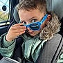 Arlo joined the competition — help win amazing prizes! child, car_seat, sunglasses, green_jacket, fur_hood, hand, face, eyes, seatbelt, window, car_interior, playful, young_child, portrait, casual, winter_clothing, cute, smile, seat, reflection