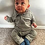 toddler, child, baby, sitting, gray_clothing, blue_socks, carpet, indoor, curious, expression, face, head, person, wall, floor, casual, young_child, small_hands, cute, portrait