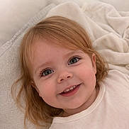 Naya a rejoint le concours — aidez-le/la à gagner de superbes lots ! toddler, child, smile, face, blond_hair, blue_eyes, white_clothing, blanket, soft_texture, indoors, cozy, happy, portrait, cute, young_child, laying_down, close_up, innocence, comfort, gentle_lighting