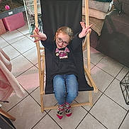 Maëlle participe au concours pour gagner de l'argent avec cette photo : child, girl, glasses, black_hoodie, blue_jeans, socks, chair, indoor, smiling, happy, playful, floor_tiles, cage, blanket, couch, furniture, person, casual_clothing, home, cozy