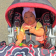 Kennedi joined the competition — help win amazing prizes! baby, child, stroller, seatbelt, headwrap, toy, outdoor, sunlight, pavement, colorful, patterned, clothing, infant, cute, portrait, seat, sitting, serious, young_child, person