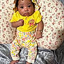 baby, child, infant, yellow_clothing, floral_hat, floral_pants, pillow, blanket, fabric, portrait, indoors, cute, smiling, person, skin, headwear, foot, hand, bracelet, sitting