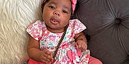 Daymira is registered to the contest to win money with this photo: baby, child, infant, pink_clothing, headband, purse, couch, plush_pillow, floral_pattern, tufted_furniture, sitting, cute, accessory, indoors, portrait, smiling, happy, toddler, young_child, cozy