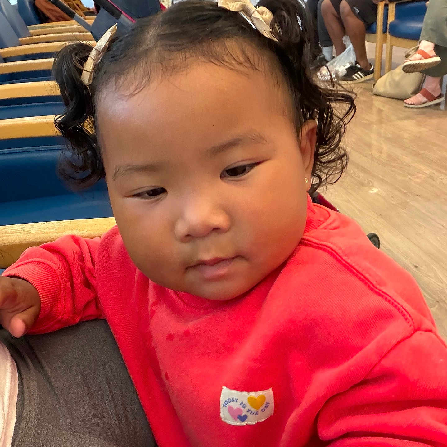 Tyclynn is registered to the contest to win money with this photo: background, candid, casual_clothing, chairs, child, curly_hair, earrings, expression, face, indoor, people, person, pigtails, red_sweatshirt, seated, stroller, toddler, waiting, waiting_room, wood_floor