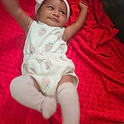 L'Eylah is registered to the contest to win money with this photo: baby, infant, child, smiling, headband, white_clothing, strawberry_pattern, red_blanket, blanket, soft_texture, lying_down, happy, cute, indoors, skin, arms_up, legs_up, sock, headwear, playful