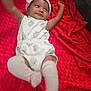 baby, infant, child, smiling, headband, white_clothing, strawberry_pattern, red_blanket, blanket, soft_texture, lying_down, happy, cute, indoors, skin, arms_up, legs_up, sock, headwear, playful