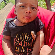 L'Eylah is registered to the contest to win money with this photo: baby, child, closeup, cute, daytime, expression, face, grass, hand, infant, onesie, outdoor, person, red_blanket, sitting, skin, summer, sunlight, text_on_clothing, young
