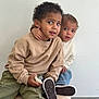 Eyden a rejoint le concours — aidez-le/la à gagner de superbes lots ! bond, candid, child, curly_hair, cute, expression, face, indoor, neutral_background, pacifier, pants, person, playful, portrait, seated, shoes, sibling, sweater, toddler, young_child