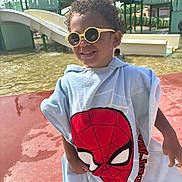 Cameron participe au concours pour gagner de l'argent avec cette photo : child, smiling, sunglasses, curly_hair, towel, spiderman, water_park, slide, playground, outdoor, sunny, happy, water, pavement, summer, person, fun, recreation, clothing, leisure
