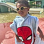 child, smiling, sunglasses, curly_hair, towel, spiderman, water_park, slide, playground, outdoor, sunny, happy, water, pavement, summer, person, fun, recreation, clothing, leisure