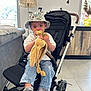 bucket_hat, casual_clothing, child, clock, couch, cute, floor_tiles, furniture, hat, indoor, jeans, lamp, living_room, pacifier, person, plush_toy, sneakers, stroller, toddler, window