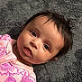 Selina is registered to the contest to win money with this photo: baby, infant, child, pink_clothing, purple_flower_pattern, carpet, floor, lying_down, portrait, face, eyes, hair, cute, indoors, soft_texture, young_child, looking_up, expression, cozy, closeup