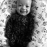 Hudson is registered to the contest to win money with this photo: baby, smiling, infant, onesie, cushion, koala_pattern, lying_down, face, happy, child, portrait, black_and_white, cute, indoor, baby_clothes, young_child, cozy, expression, baby_boy, closeup