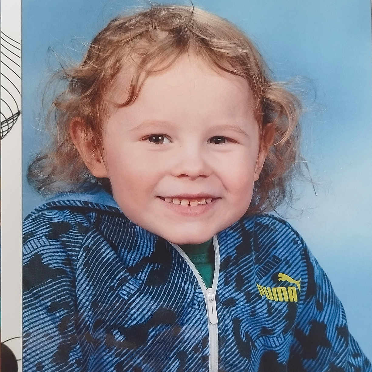 Tiago participe au concours pour gagner de l'argent avec cette photo : blue_background, blue_jacket, casual_clothing, child, curly_hair, cute, doodle_sketch, face, framed_photo, happy, headshot, indoor, patterned_border, person, portrait, puma_logo, smiling, studio_photo, young_child, zipper