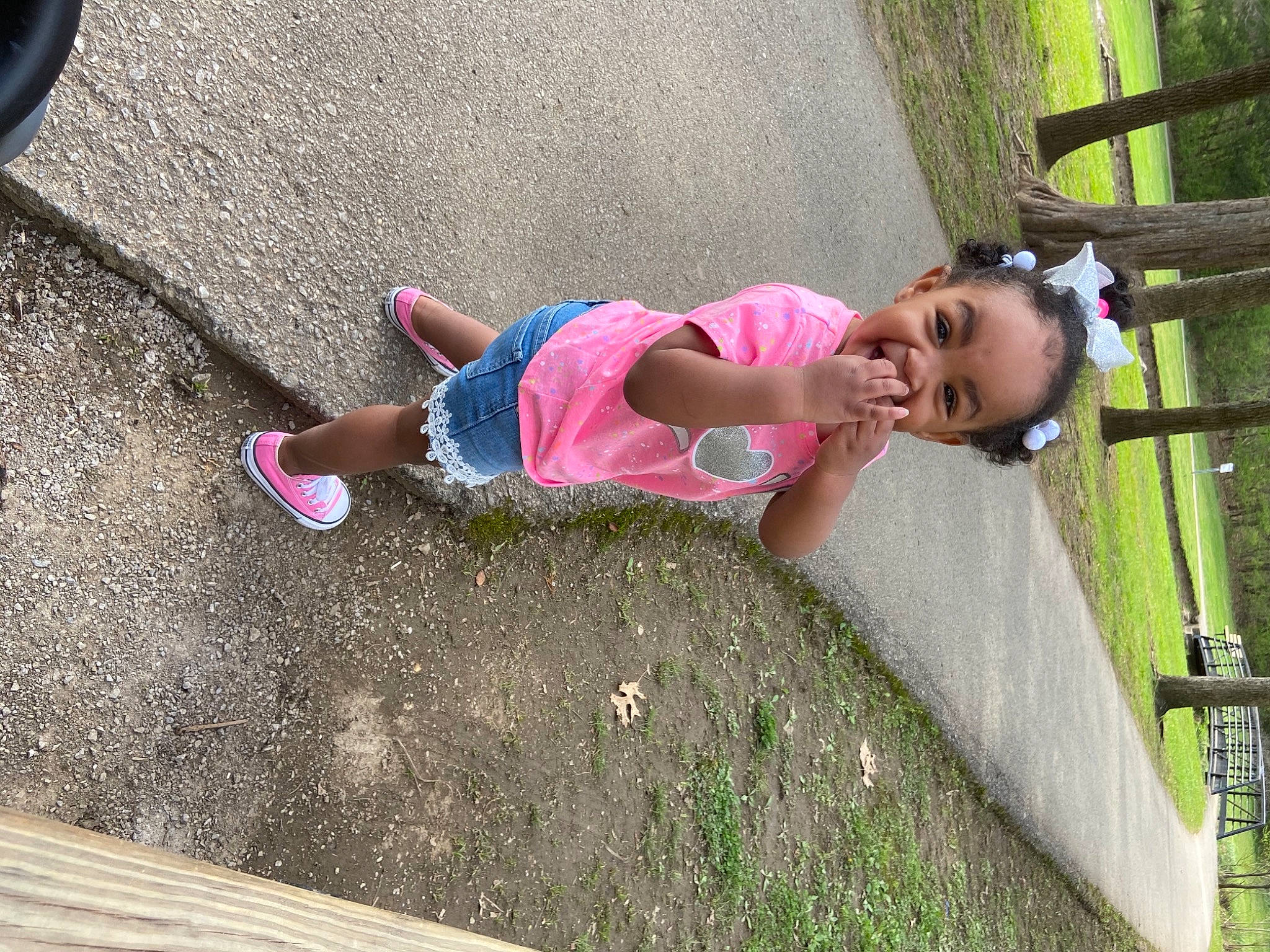 Ava is registered to the contest to win money with this photo: asphalt, automotive_tire, baby, baby_toddler_clothing, child, foot, fun, grass, human_leg, leisure, magenta, person, pink, recreation, road_surface, sidewalk, thigh, tire, toddler, tree