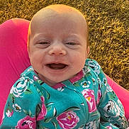 Avery joined the competition — help win amazing prizes! baby, smiling, infant, child, outdoor, grass, sunlight, pink, floral_clothing, jacket, happy, face, cute, portrait, sitting, young_child, nature, daylight, warm_light, person