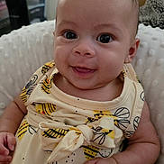 Willow is registered to the contest to win money with this photo: baby, infant, smiling, cute, yellow_dress, bee_pattern, soft_cushion, indoors, happy, portrait, child, person, closeup, cheerful, young, skin, hand, head, eyes, expression