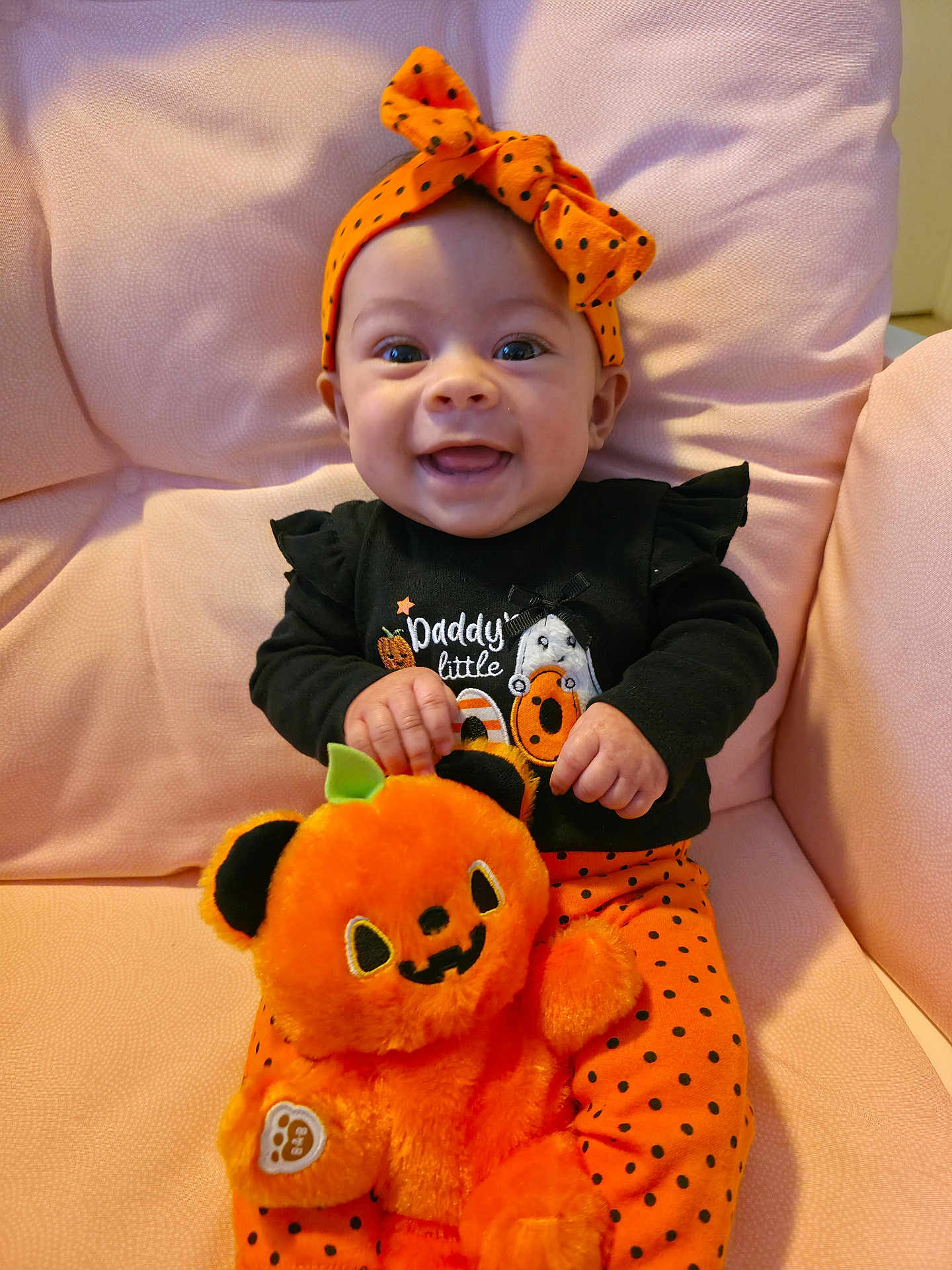 Willow joined the competition — help win amazing prizes! baby, child, smiling, orange_headband, polka_dot, black_shirt, plush_toy, pumpkin, halloween, chair, pink_background, happy, cute, indoor, portrait, sitting, headband, toy, clothing, person
