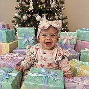Willow joined the competition — help win amazing prizes! baby, child, smiling, christmas_tree, presents, gift_boxes, holiday, festive, ribbon, bow, headband, indoors, celebration, happy, cute, sitting, decorations, winter, holiday_lighting, joyful