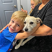 Sadie is registered to the contest to win money with this photo: boy, dog, child, pet, hug, family, woman, glasses, smartphone, indoor, affection, seated, casual, closeup, blond_hair, white_dog, black_clothing, smile, warmth, candid