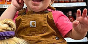 Mavis is registered to the contest to win money with this photo: bottles, child, clothing, cute, face, grocery_aisle, hair, hand, happy, hot_sauce, overalls, person, pink_shirt, portrait, retail, shelf, shopping, smiling, store, toddler