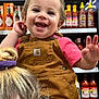 Mavis is registered to the contest to win money with this photo: toddler, child, smiling, overalls, pink_shirt, store, grocery_aisle, hot_sauce, bottles, shelf, happy, person, portrait, cute, retail, shopping, hand, hair, face, clothing