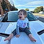 toddler, child, car, hood, white_car, smiling, happy, outdoor, street, blue_sky, trees, buildings, casual_clothing, barefoot, daytime, person, baby, joyful, vehicle, sitting