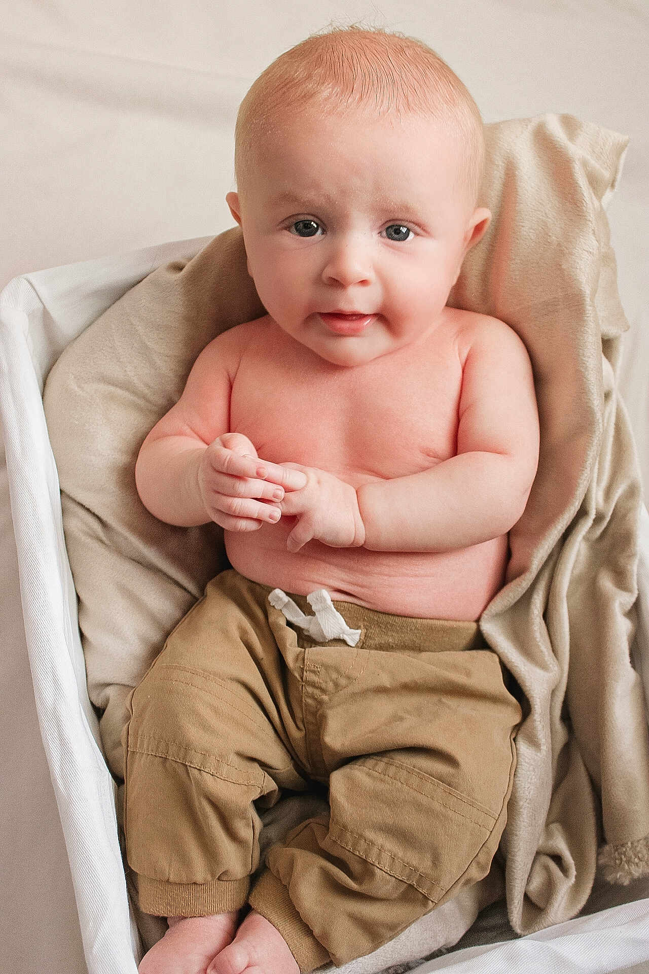 Clayton is registered to the contest to win money with this photo: baby, child, infant, portrait, face, hands, bare_chest, pants, beige, blanket, basket, sitting, cute, soft_lighting, indoor, skin, expression, young, newborn, comfort