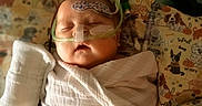 Carter is registered to the contest to win money with this photo: baby, swaddled, blanket, medical_tubes, nasal_cannula, monitoring_patch, sleeping, infant, hospital, cute, child, pacifier, face, healthcare, resting, colorful_blanket, pattern, dog_illustrations, closeup, newborn