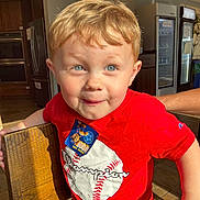 Colton joined the competition — help win amazing prizes! child, boy, red_shirt, baseball_graphic, blond_hair, blue_eyes, smile, indoor, chair, wood, kitchen, refrigerator, sunlight, shadow, person, casual_clothing, cute, portrait, playful, toddler