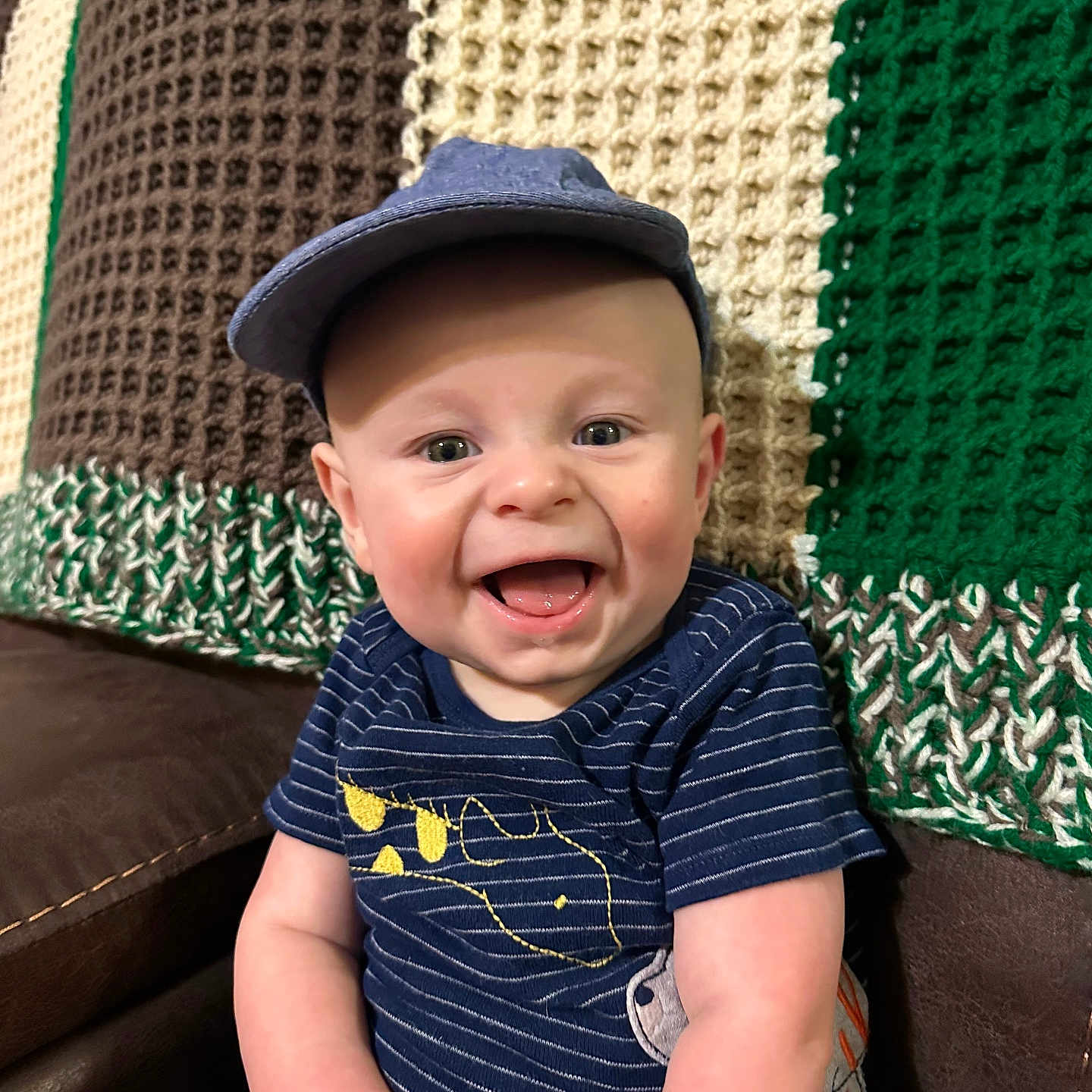 Kenton joined the competition — help win amazing prizes! baby, blue_clothing, cap, cheerful, child, clothing, couch, cute, face, happy, hat, indoors, infant, knitted_blanket, person, portrait, sitting, smiling, striped, young_child