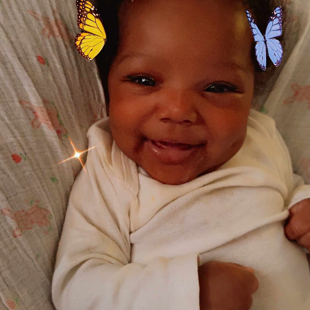 Sevyn is registered to the contest to win money with this photo: baby, blanket, butterflies, child, closeup, cozy, cute, digital_effects, dimples, face, hands, happy, indoors, infant, lying_down, onesie, portrait, skin, smiling, young_child