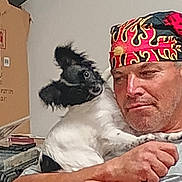 Izzy is registered to the contest to win money with this photo: man, dog, pet, indoor, bandana, black_and_white, curious, holding, expression, casual, furniture, cardboard_box, sitting, portrait, animal, person, face, fur, human, closeup