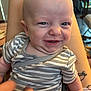 baby, infant, striped_clothing, smile, face, person, arm, tattoo, legs, indoor, furniture, background, expression, cute, skin, holding, closeup, cheeky, young_child, happy