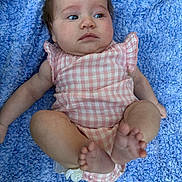 Saige joined the competition — help win amazing prizes! baby, infant, child, blue_blanket, pink_outfit, checkered_pattern, barefoot, curly_hair, spiky_hair, lying_down, soft_texture, skin, cute, expression, small_feet, indoors, portrait, one_person, clothing, relaxed