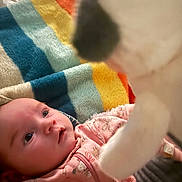 Darcy joined the competition — help win amazing prizes! baby, infant, plush_toy, pink_clothing, blanket, colorful, striped_blanket, curious, wide_eyes, soft_texture, indoor, cozy, child, cute, portrait, human, young, expression, closeup, warm