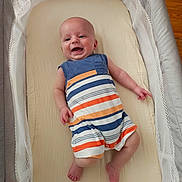 Riley is registered to the contest to win money with this photo: baby, infant, smiling, romper, striped_clothing, bassinet, crib, bedding, mesh_sides, mobile, happy, child, indoors, flooring, wood_floor, cute, portrait, newborn, person, sleeping_area
