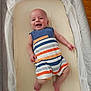 baby, infant, smiling, romper, striped_clothing, bassinet, crib, bedding, mesh_sides, mobile, happy, child, indoors, flooring, wood_floor, cute, portrait, newborn, person, sleeping_area