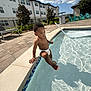 toddler, pool, water, diaper, child, outdoor, sunny, clouds, building, sidewalk, greenery, chair, fence, residential, person, foot, sky, reflection, daytime, curious