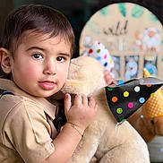 Neo is registered to the contest to win money with this photo: toddler, child, face, plush_toy, teddy_bear, party_hat, polka_dot, cuddling, portrait, indoors, soft_lighting, short_hair, brown_hair, skin, clothing, bracelet, happy, cute, celebration, background_blur