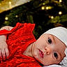 baby, background_bokeh, celebration, child, christmas_lights, closeup, cute, eyes, face, festive, flower_accessory, hand, headband, holiday, infant, lying_down, portrait, red_dress, soft_skin, warm_lighting