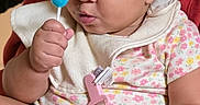 Ayla is registered to the contest to win money with this photo: baby, bib, child, curious, cute, expression, face, floral_onesie, hand, holding, indoors, infant, lollipop, looking, pacifier_clip, person, red_background, seated, skin, young