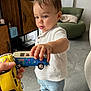 énoha participe au concours pour gagner de l'argent avec cette photo : toddler, child, toy, toy_car, hand, shirt, pants, shoe, indoor, floor, cabinet, chair, person, curious, playing, living_room, window, curtain, wood, footwear