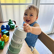 énoha a rejoint le concours — aidez-le/la à gagner de superbes lots ! toddler, child, smiling, happy, indoor, table, wood, stacking, toys, plastic, colorful, blocks, blue_shirt, shorts, window, natural_light, furniture, play, baby, seat