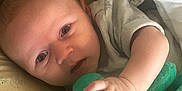 Jerry is registered to the contest to win money with this photo: baby, infant, plush_toy, green_toy, hand, face, eyes, bedding, blanket, sleeping_area, soft_toy, cute, child, person, indoors, closeup, lying_down, comfortable, expression, young