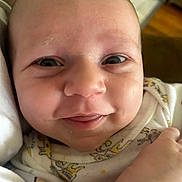Jerry is registered to the contest to win money with this photo: baby, smile, face, close_up, infant, onesie, hand, expression, cute, skin, eyes, tongue, joy, child, person, newborn, happy, portrait, indoors, cozy