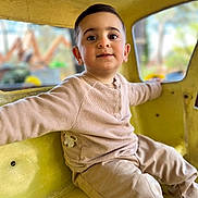 Mickael a rejoint le concours — aidez-le/la à gagner de superbes lots ! child, toddler, boy, sitting, yellow, playground, indoor, clothing, long_sleeve, pants, curious, face, smile, eyes, hair, window, background_blur, casual, happy, cute